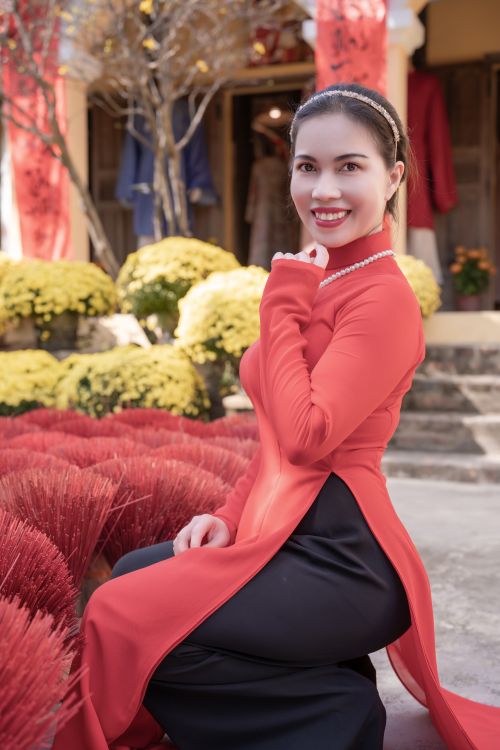Free Happy woman in a red Ao Dai amidst a vibrant, festive setting. Perfect for cultural celebration themes. Stock Photo