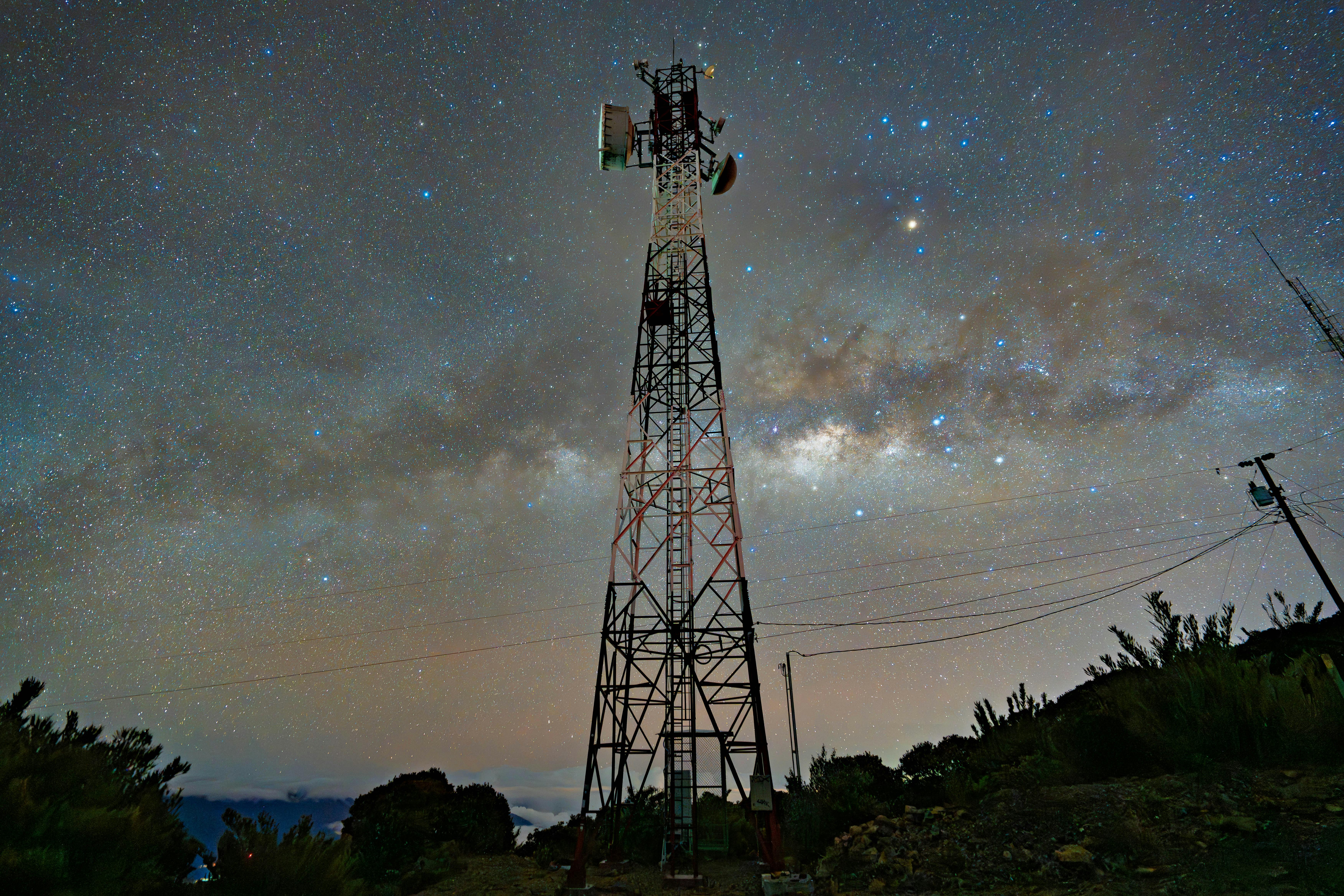 A communication tower silhouetted against a stunning starry night sky with the Milky Way.