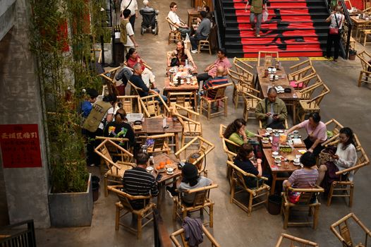 Overhead view of an indoor café with patrons seated at bamboo tables, capturing lively discussions.