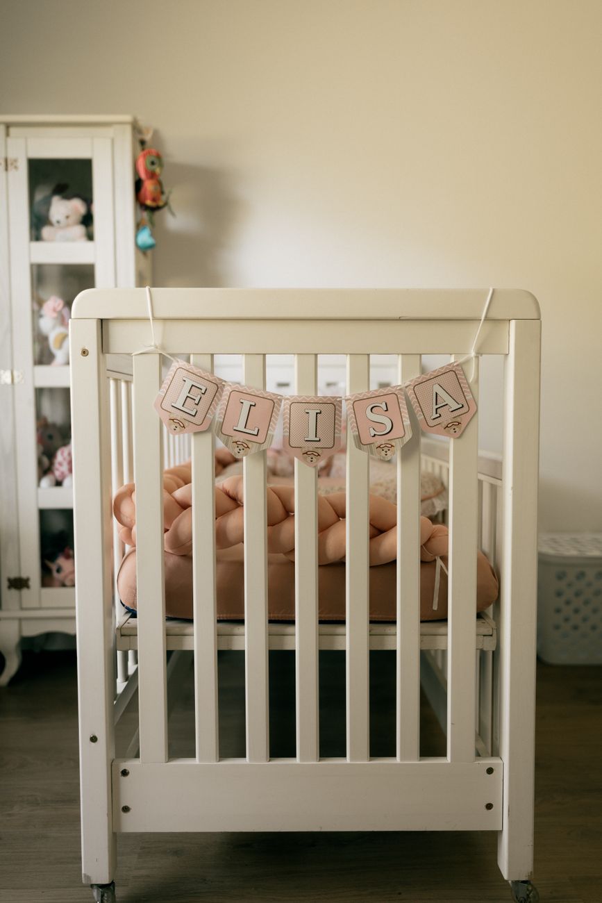 Quarto de bebê em tons neutros com berço branco decorado com faixa de nome e bichinhos de pelúcia