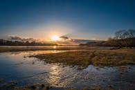 宁静的日出下，阳光映照着河流与郁郁葱葱的草地，天空晴朗