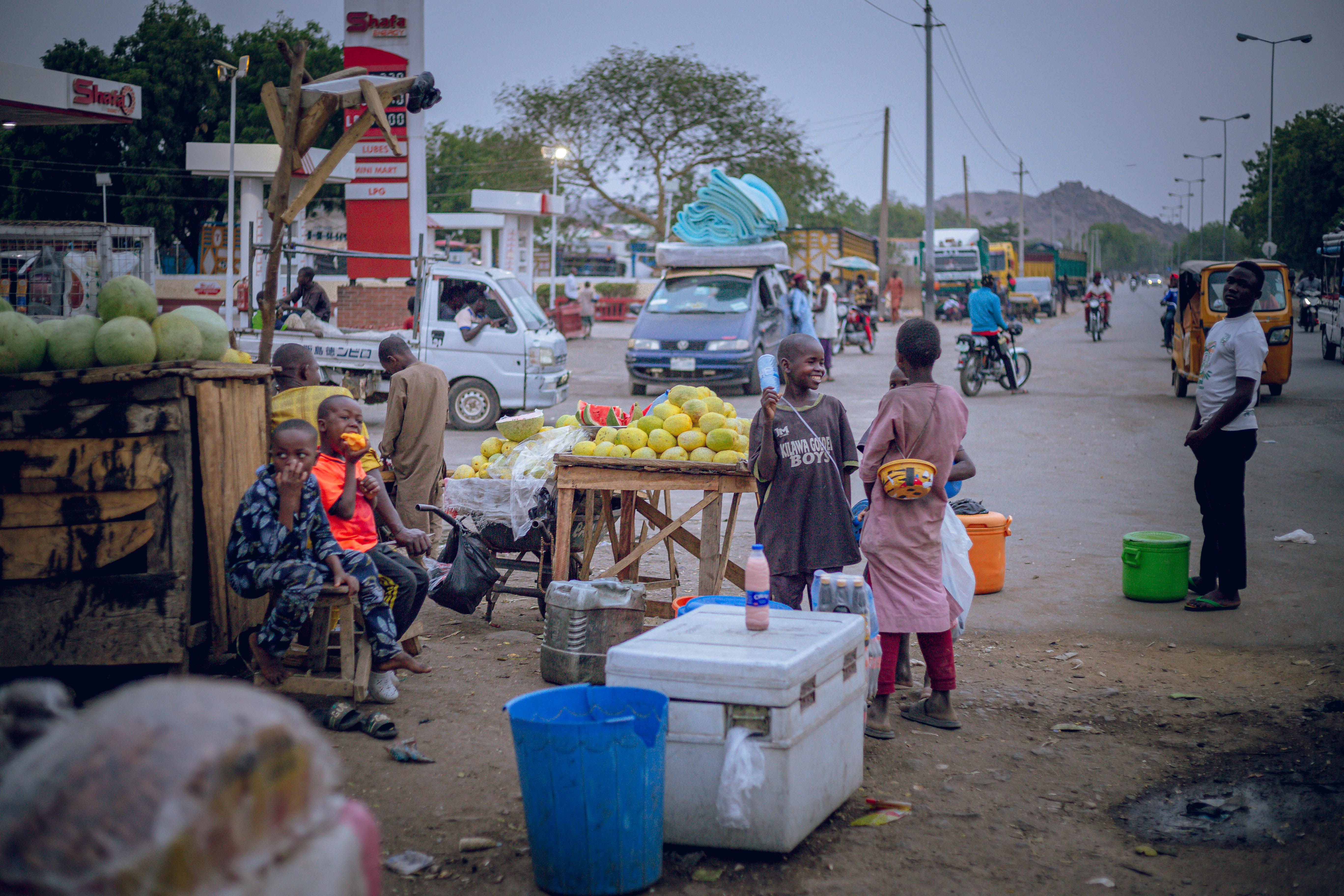 Busy street market with vendors selling produce, lively atmosphere at dusk.