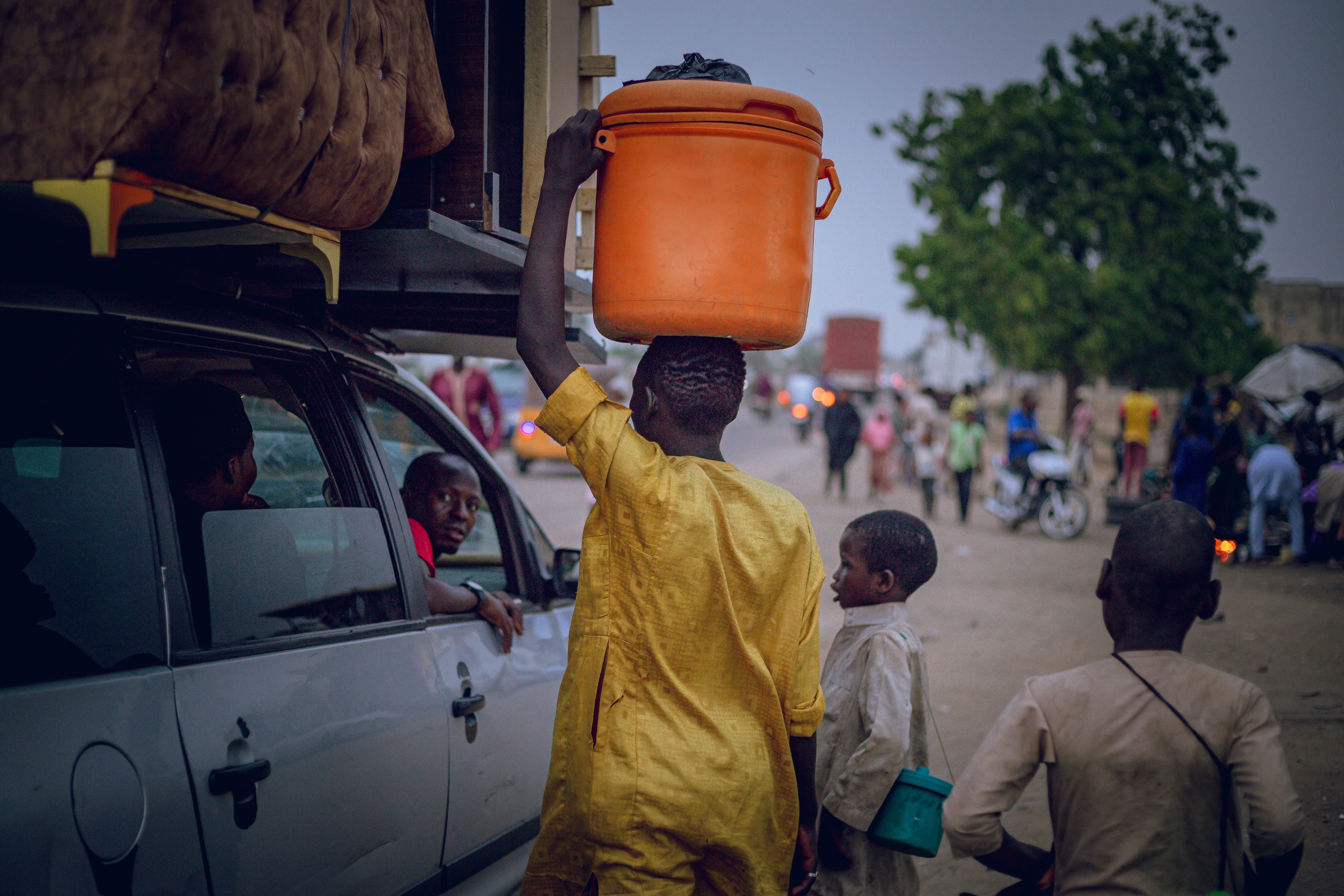 Young boy in vibrant yellow carries an orange container on a busy street, showcasing daily life in Africa.
