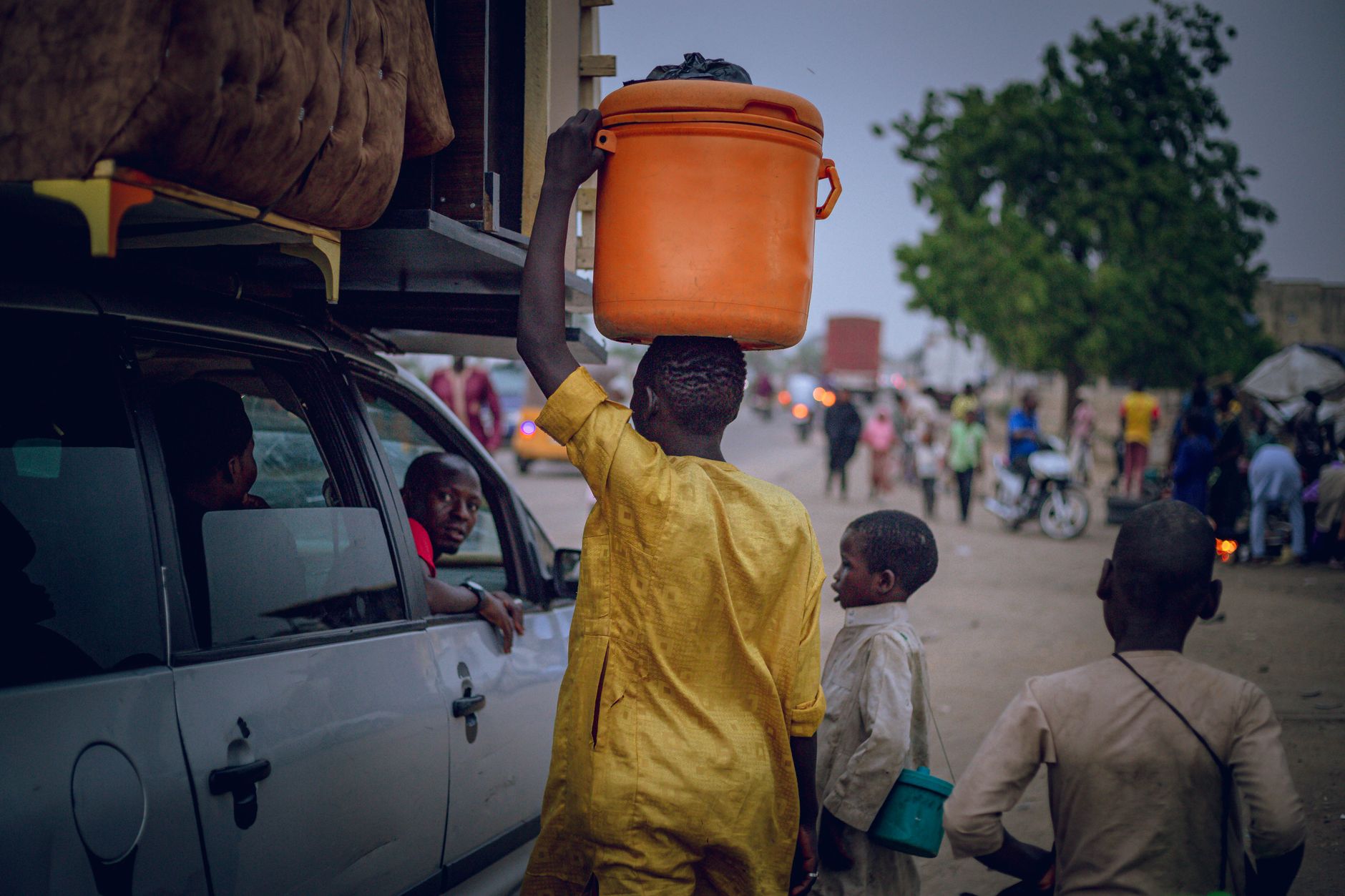 Young boy in vibrant yellow carries an orange container on a busy street, showcasing daily life in Africa.