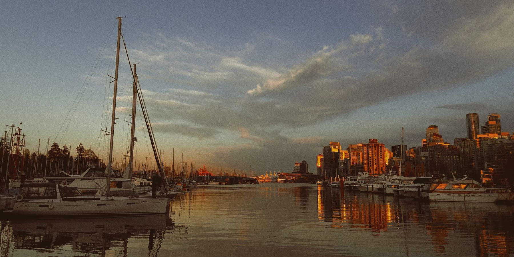 A stunning view of boats docked at a marina during golden hour, with the Vancouver skyline bathed in warm sunset light.