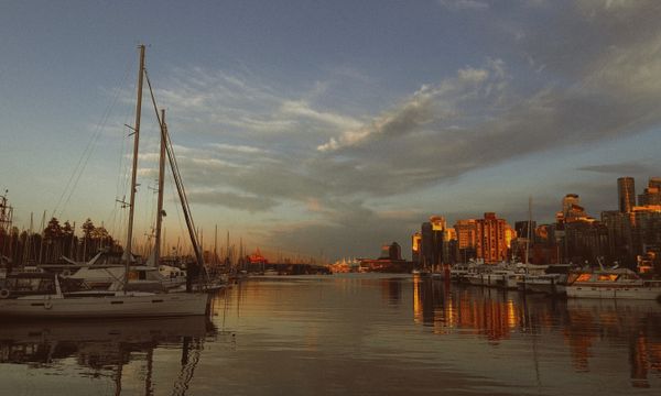 A stunning view of boats docked at a marina during golden hour, with the Vancouver skyline bathed in warm sunset light.