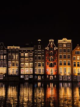 Night view of Amsterdam canal houses reflected in water, showcasing classic architecture.