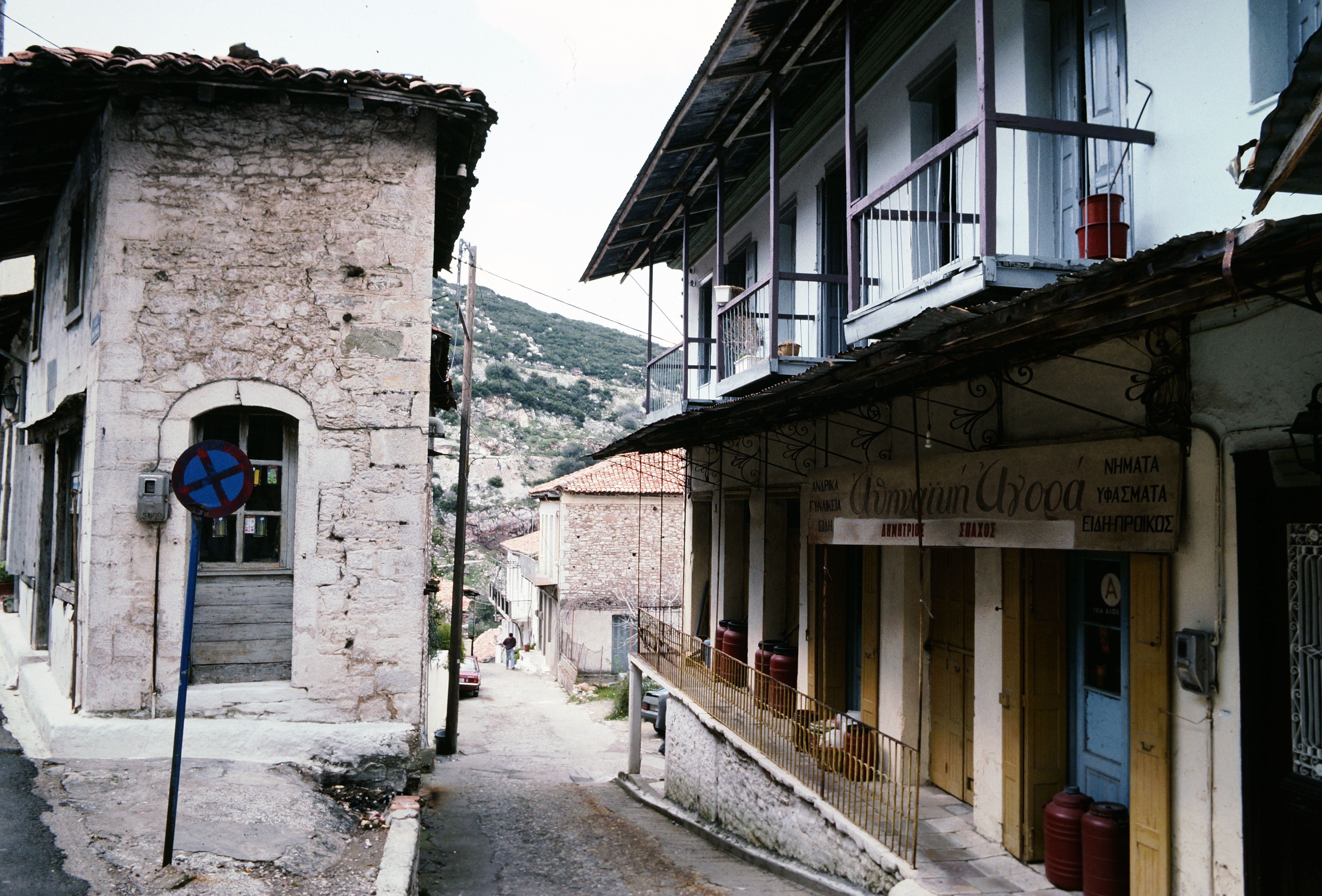 Picturesque street scene in a quaint Greek village featuring rustic stone houses and scenic mountain backdrop.