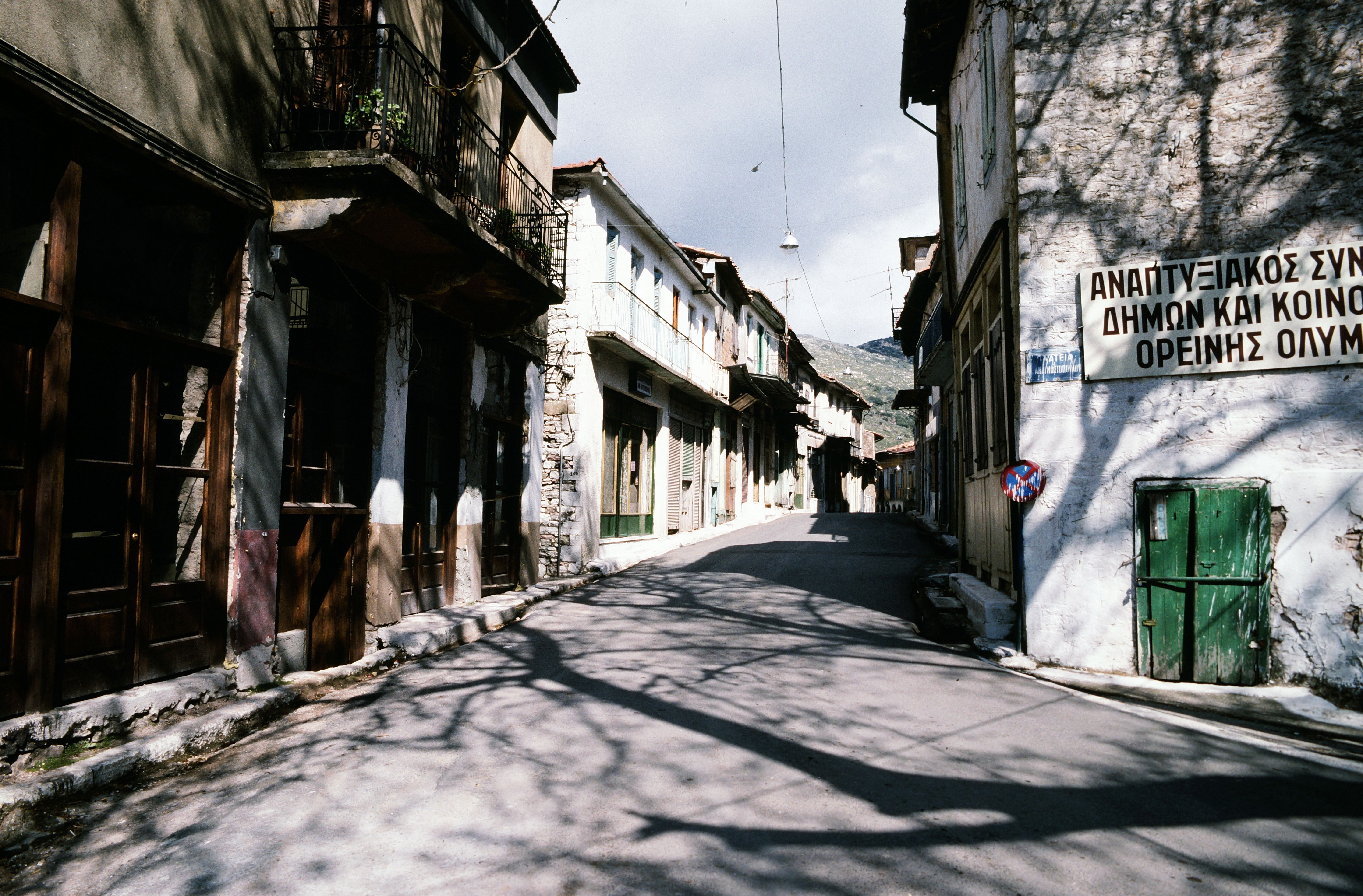 Charming sunlit street in a traditional Greek village with rustic architecture and shadows.