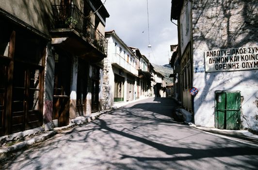 Charming sunlit street in a traditional Greek village with rustic architecture and shadows.