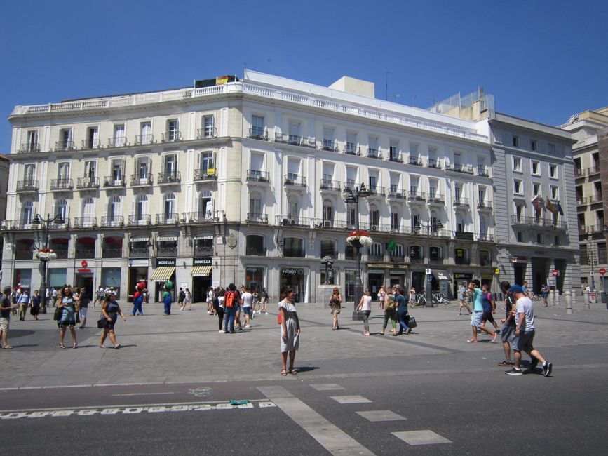 Una escena vibrante en la Puerta del Sol en Madrid con peatones en un brillante día de verano.