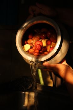 Hands holding a pot with fruits for a traditional infusion recipe.
