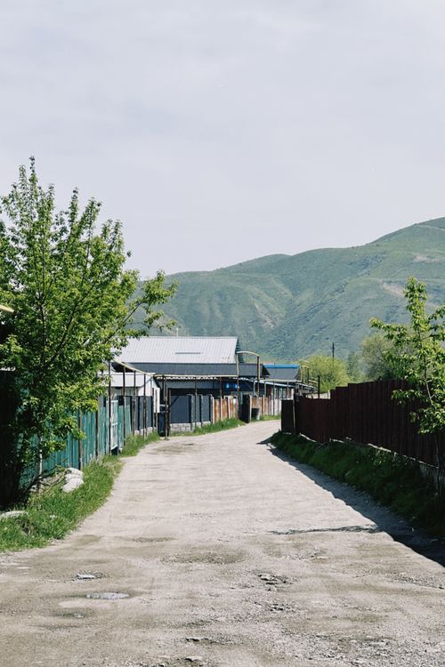Free Rustic village road in Talgar, showcasing scenic green hills and traditional houses. Stock Photo