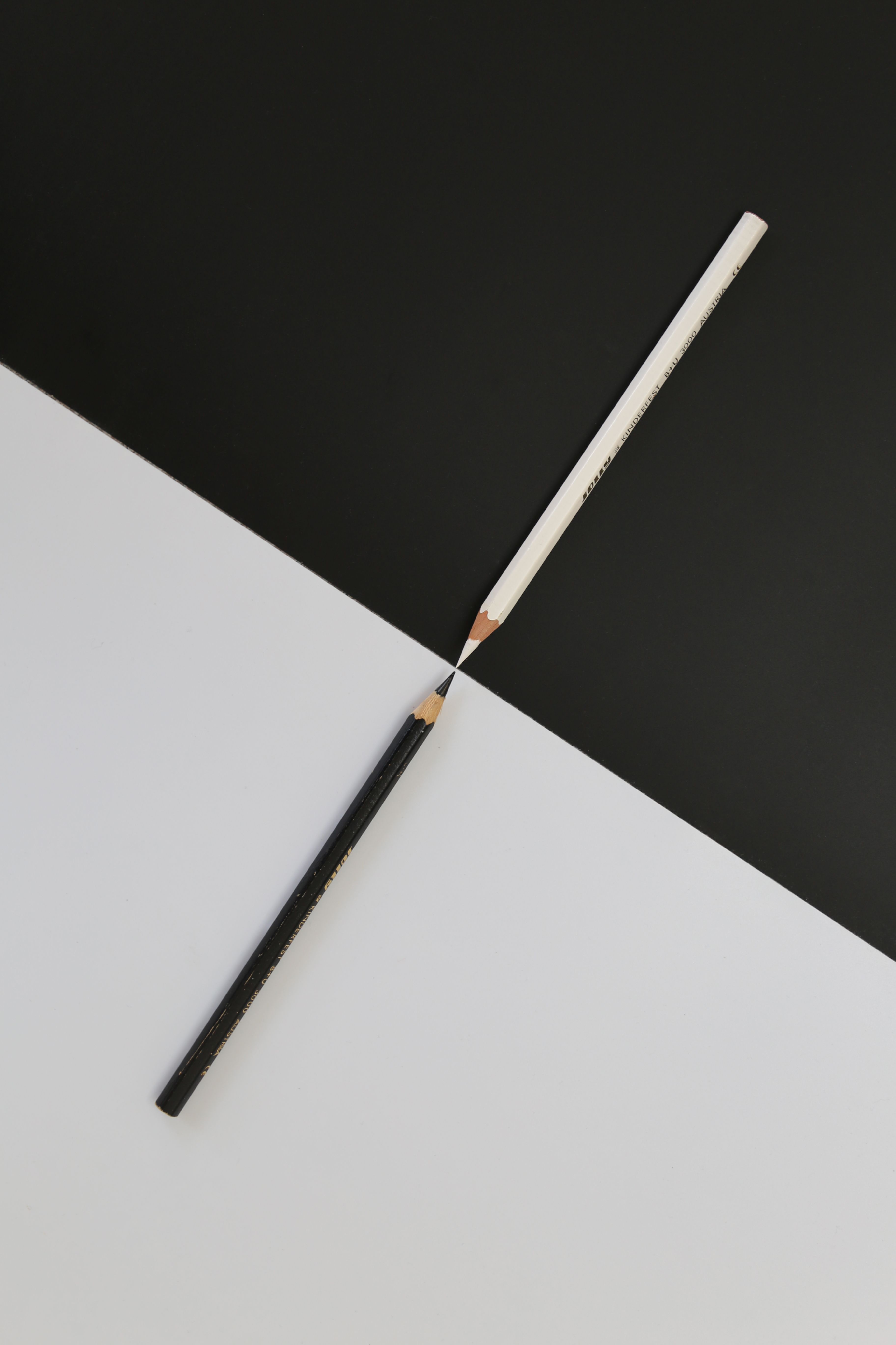 Two pencils intersecting on a black and white geometric background, highlighting minimalism and symmetry.