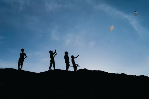 Silhouettes of children flying kites against evening sky in Chattogram, Bangladesh. A picturesque and playful scene.