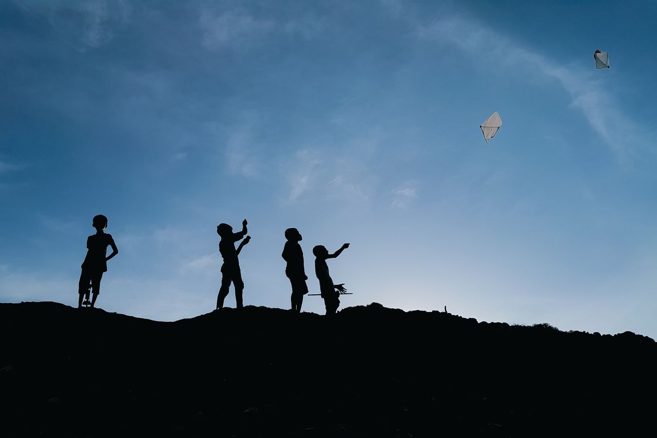 silhouettes of children flying kites against evening sky in chattogram