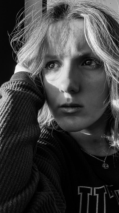 Free A compelling black and white portrait of a young woman deep in thought, emphasizing light and shadow contrast. Stock Photo