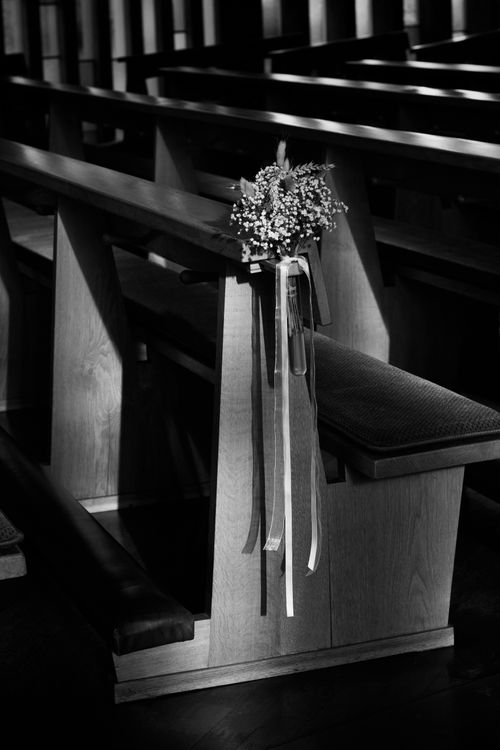 Free A church pew decorated with flowers and ribbons in monochrome lighting, creating a serene wedding atmosphere. Stock Photo
