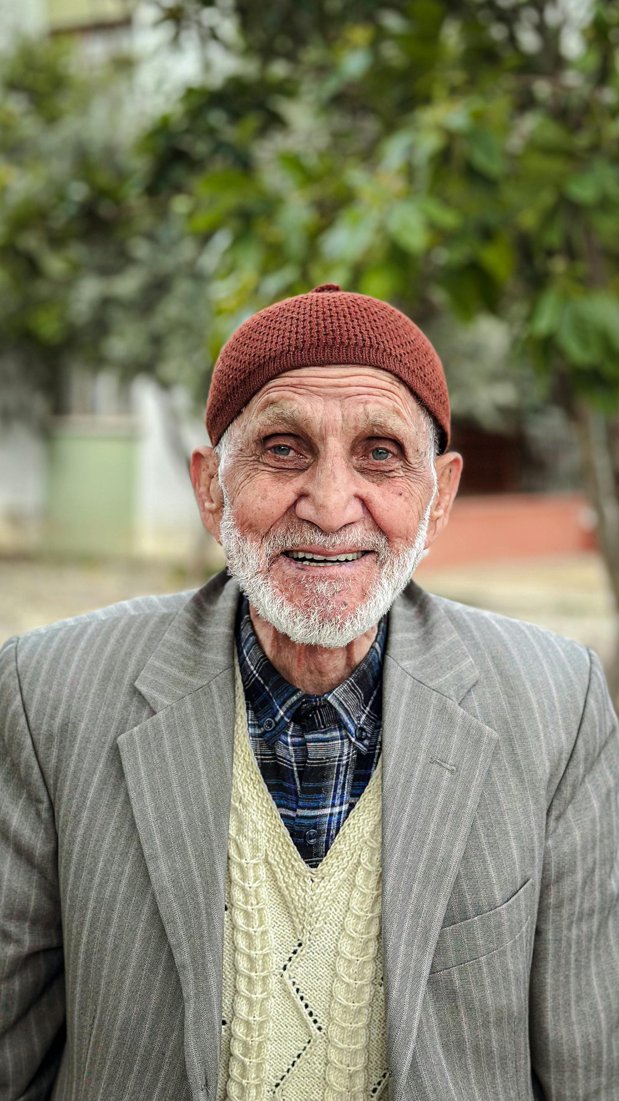 Portrait of an elderly man wearing a knit cap, smiling warmly in an outdoor autumn setting. Lifestyle theme.