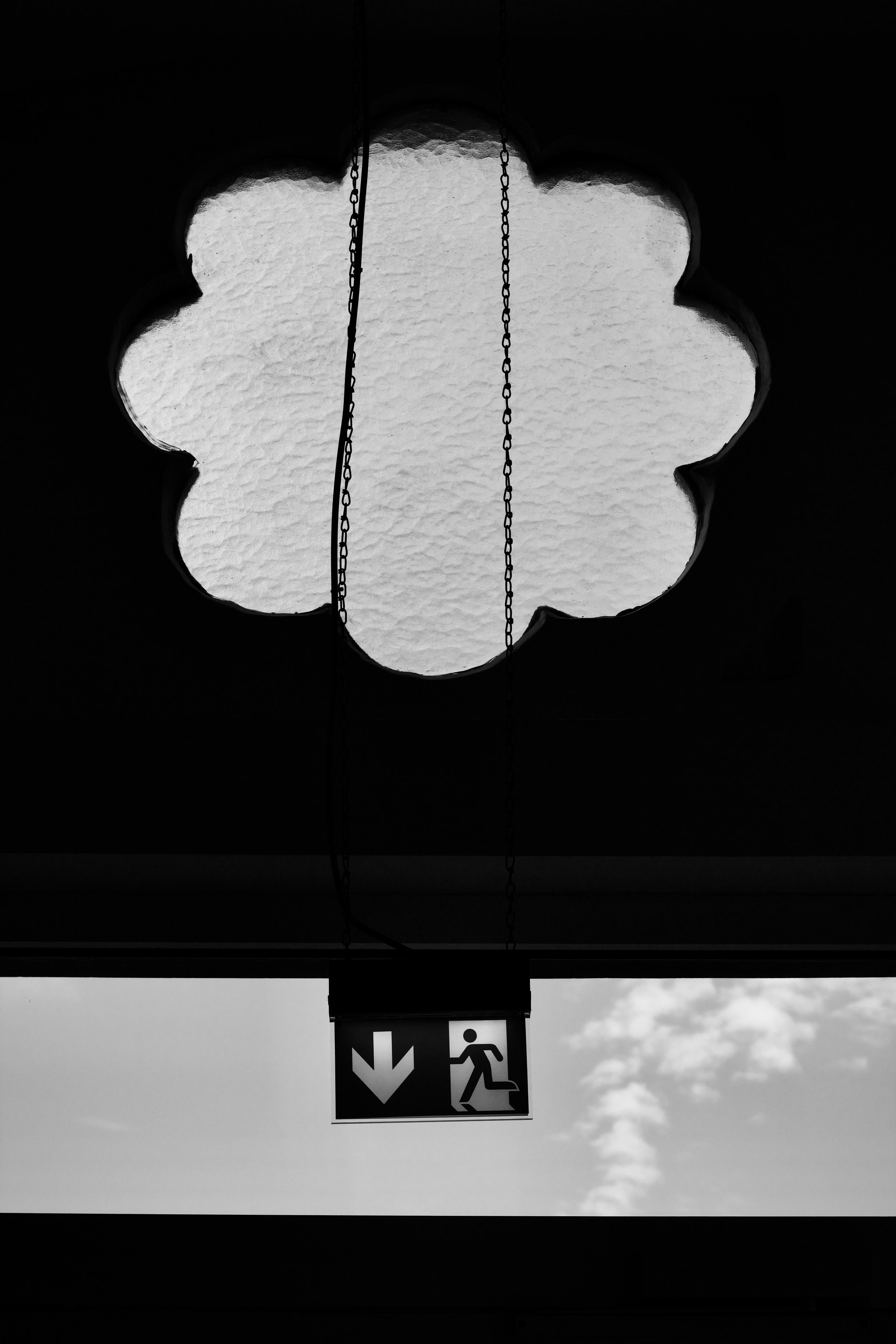 A black and white photo of an emergency exit sign beneath a decorative window, featuring a minimalist layout.