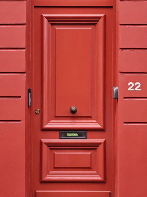 Stylish red door with ornate paneling and number 22, epitomizing classic architecture.