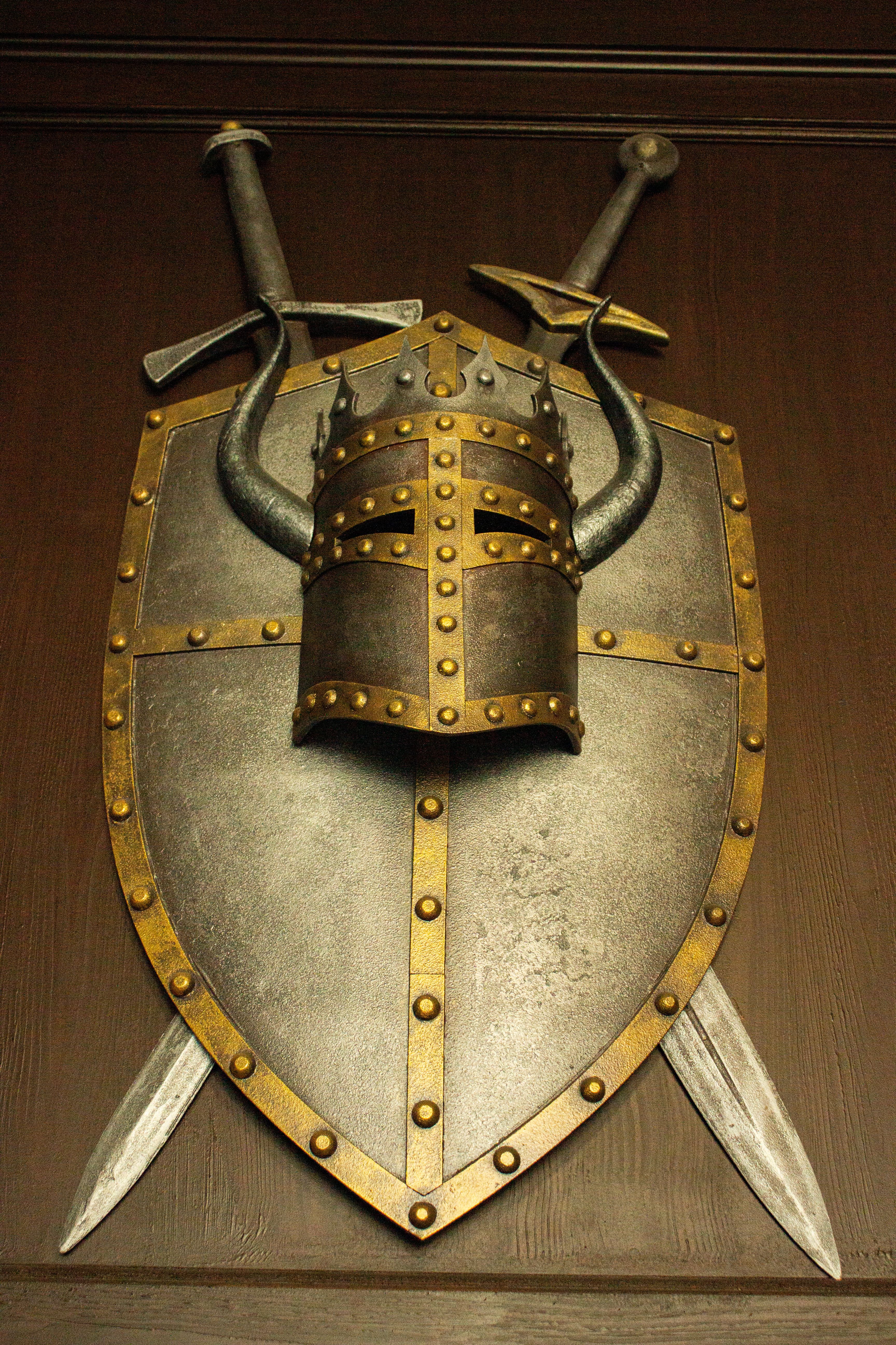 Metallic medieval helmet and shield with swords displayed on a wooden wall, evoking historical themes.