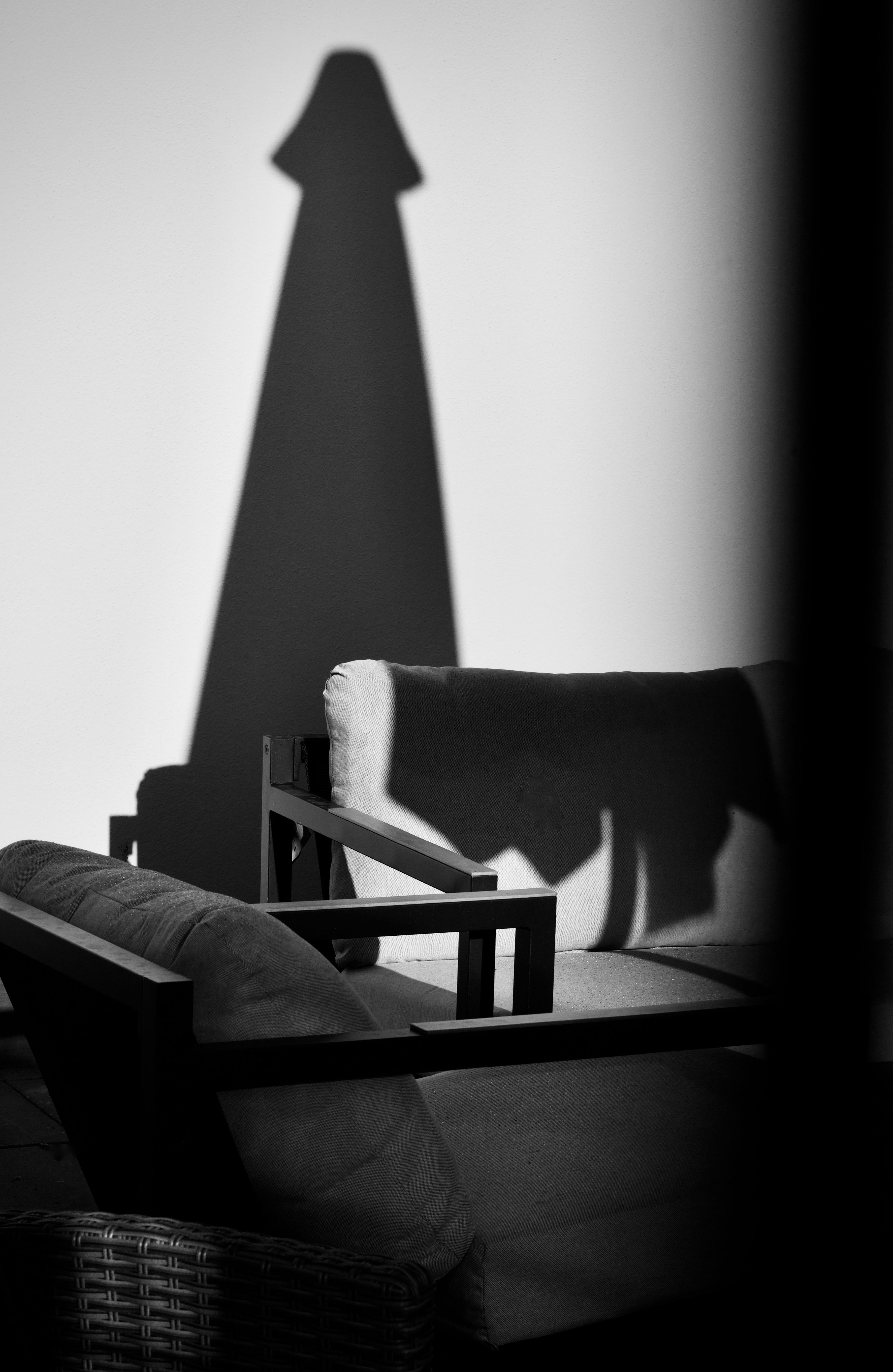 Black and white photo of lamp shadow cast on wall with chair in foreground.