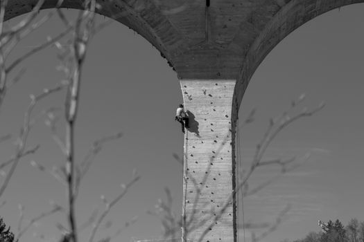 A climber scales a bridge pillar with climbing holds in a striking black and white image.