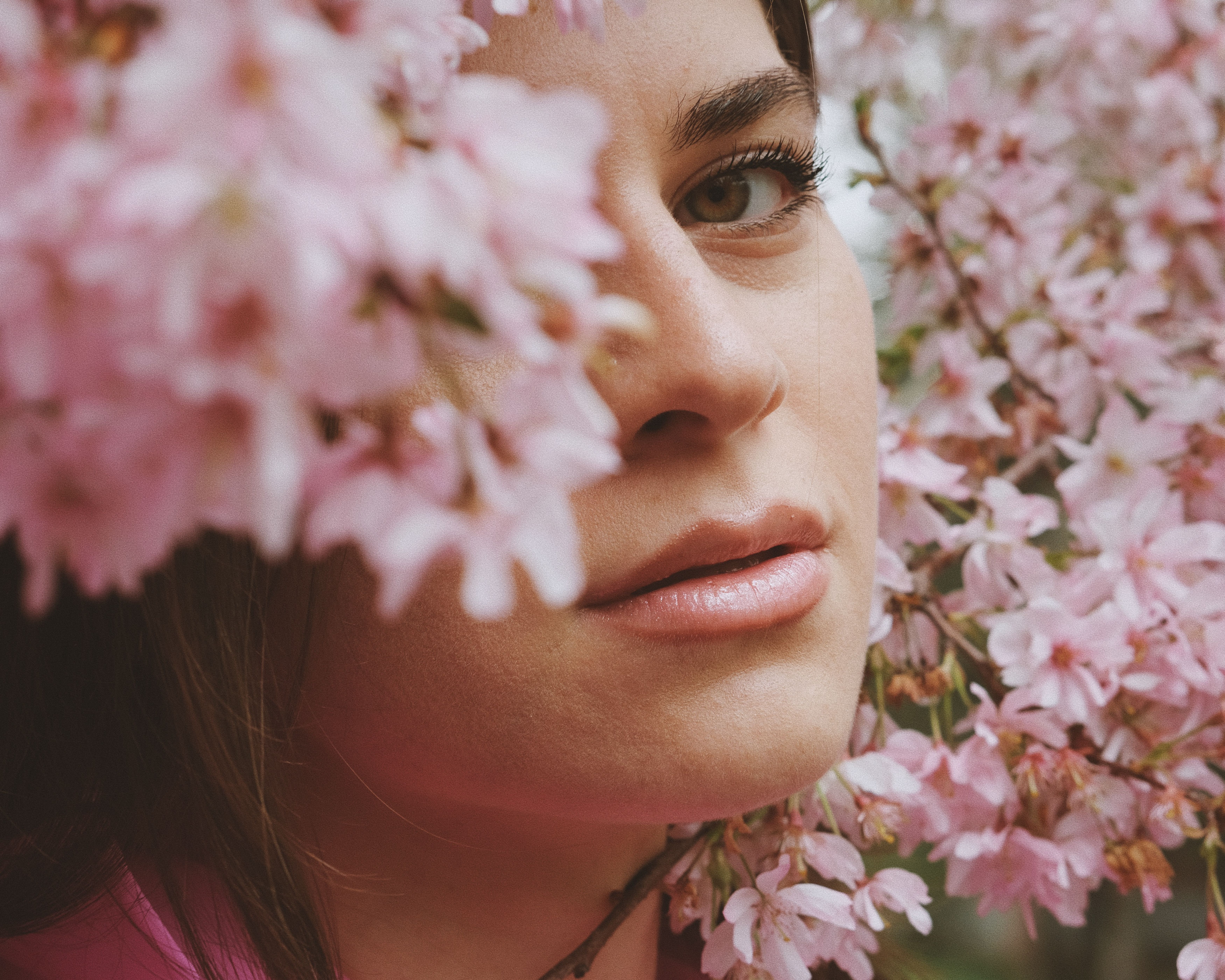 Close-up portrait of a woman surrounded by blooming cherry blossoms, capturing a serene springtime moment.