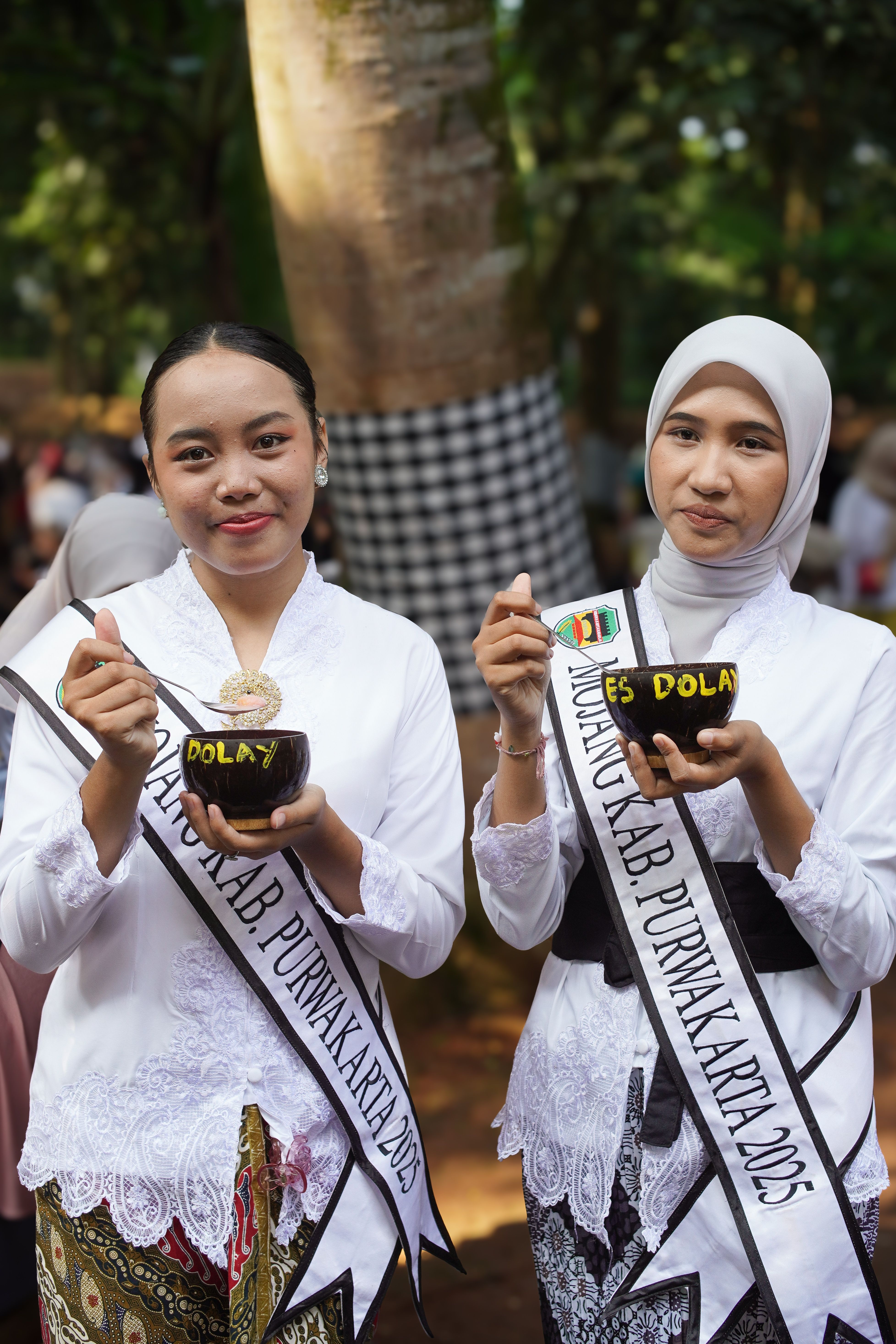 Two women in traditional attire enjoying 'es dolet' during a cultural event in Purwakarta, Indonesia.