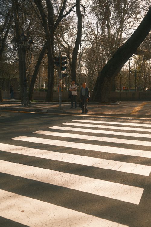 Free A serene urban crosswalk with pedestrians during sunset, casting long shadows. Stock Photo