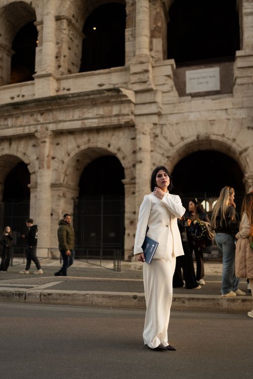Free Woman in white suit stands confidently near the historic Colosseum in Rome, Italy. Stock Photo
