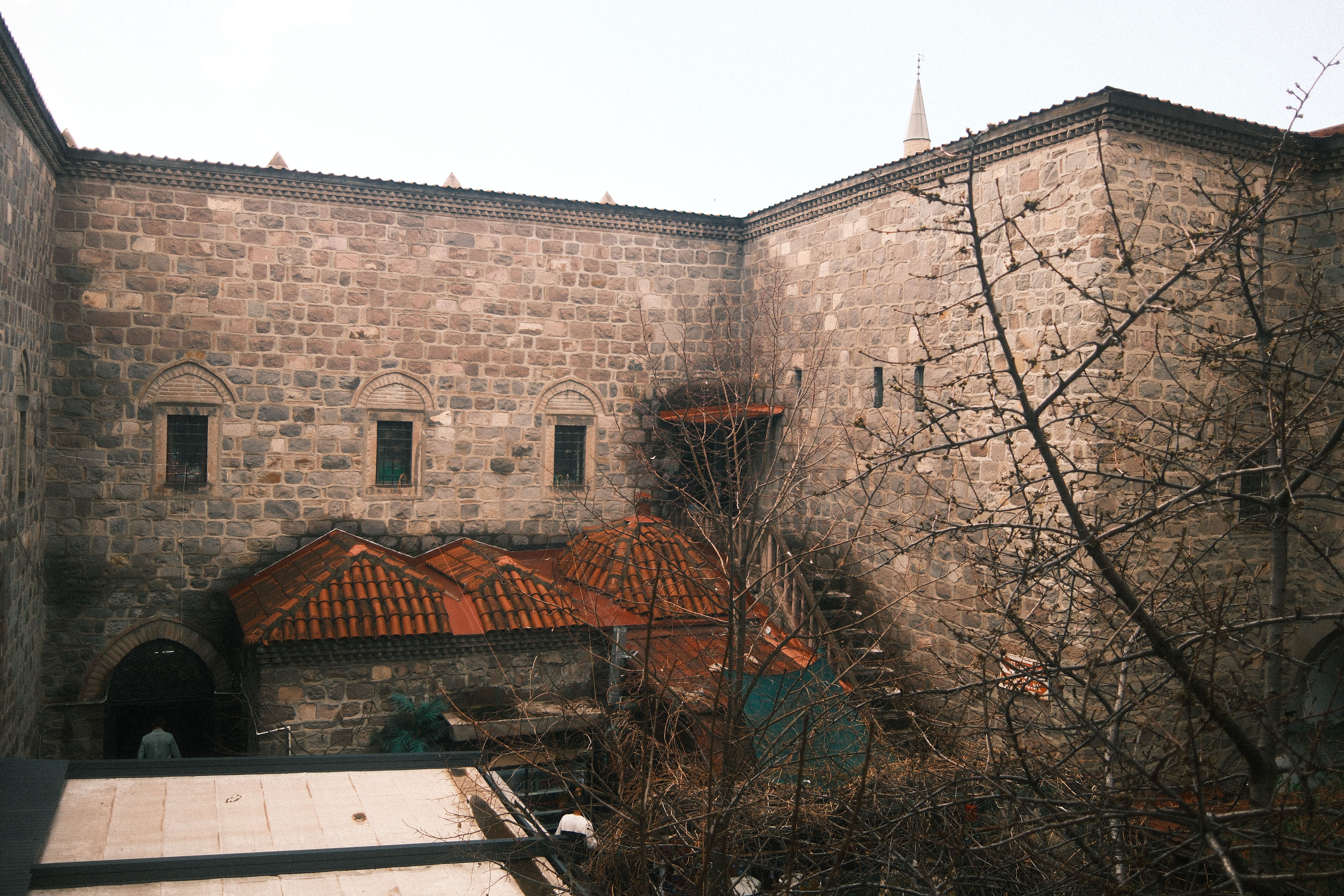 Bezpłatne Kamienny budynek z czerwonym dachem krytym dachówką, zabytkowa architektura, nagie drzewa, delikatne oświetlenie. Zdjęcie z galerii