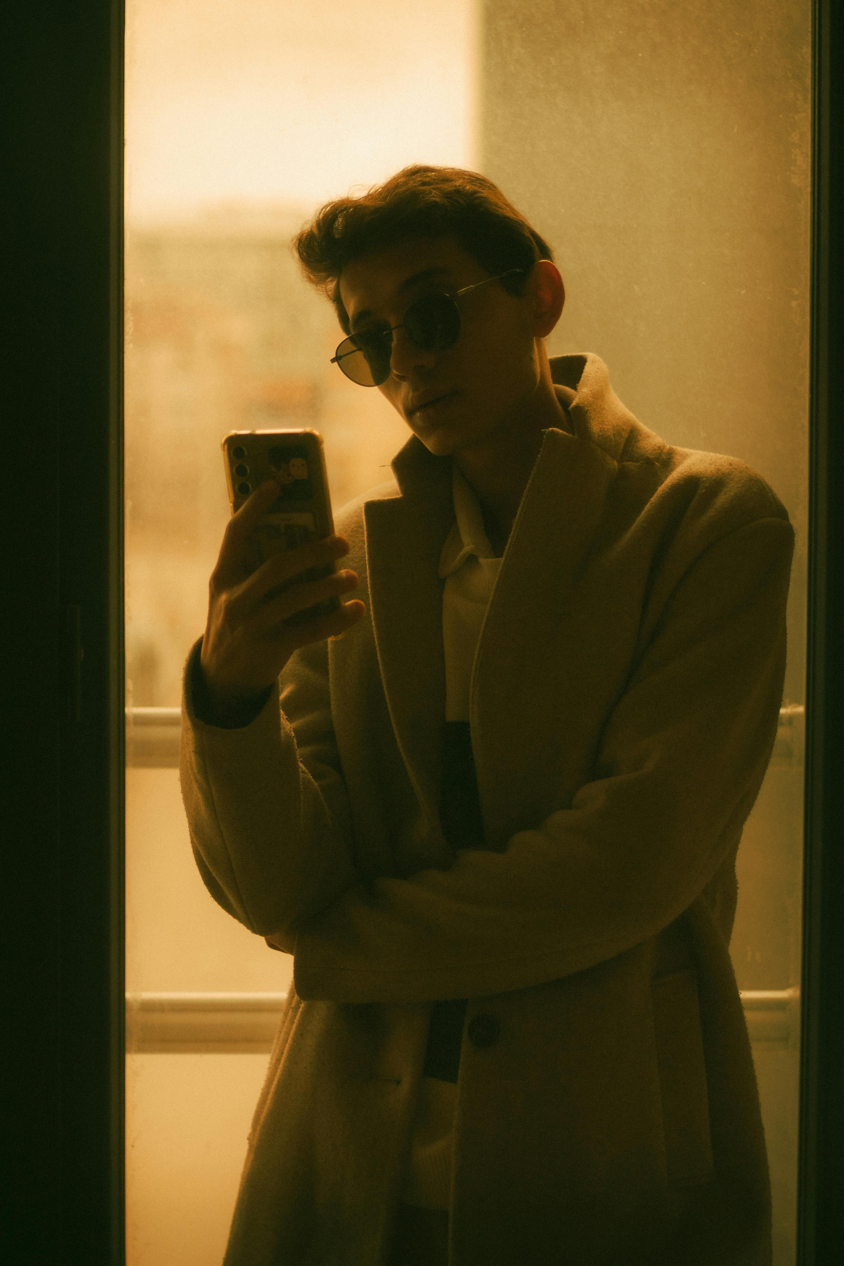 Stylish young adult in sunglasses holding a smartphone, exuding a modern and moody vibe.