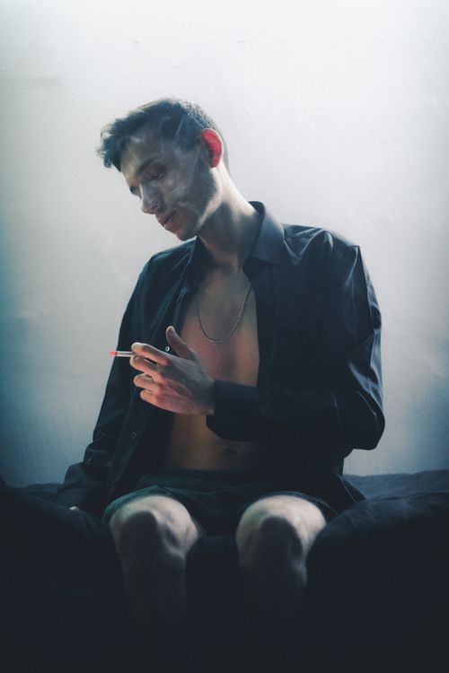 Free Young man in dramatic lighting with cigarette, exuding a moody vibe. Stock Photo