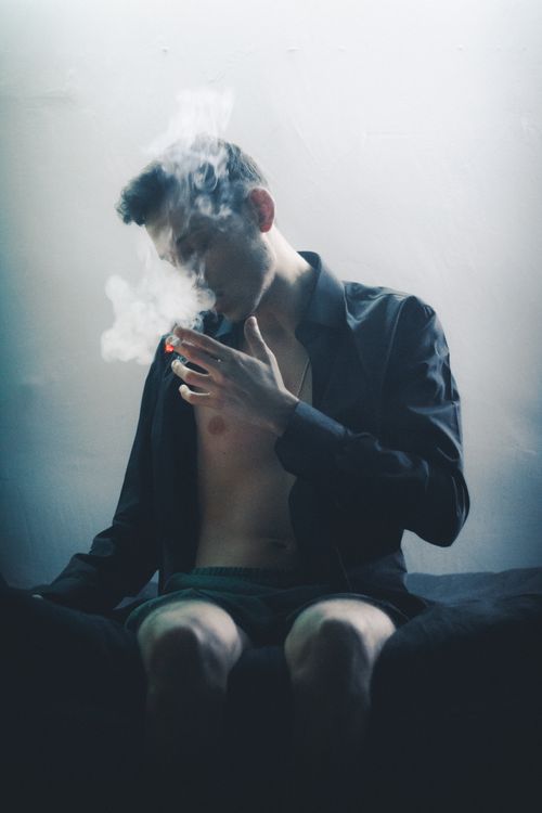 Free Artistic portrait of a man smoking indoors with dramatic lighting and smoke effect. Stock Photo