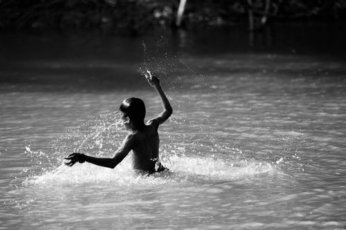 Free A child joyfully splashes in a river in Battambang Province, Cambodia, captured in black and white. Stock Photo