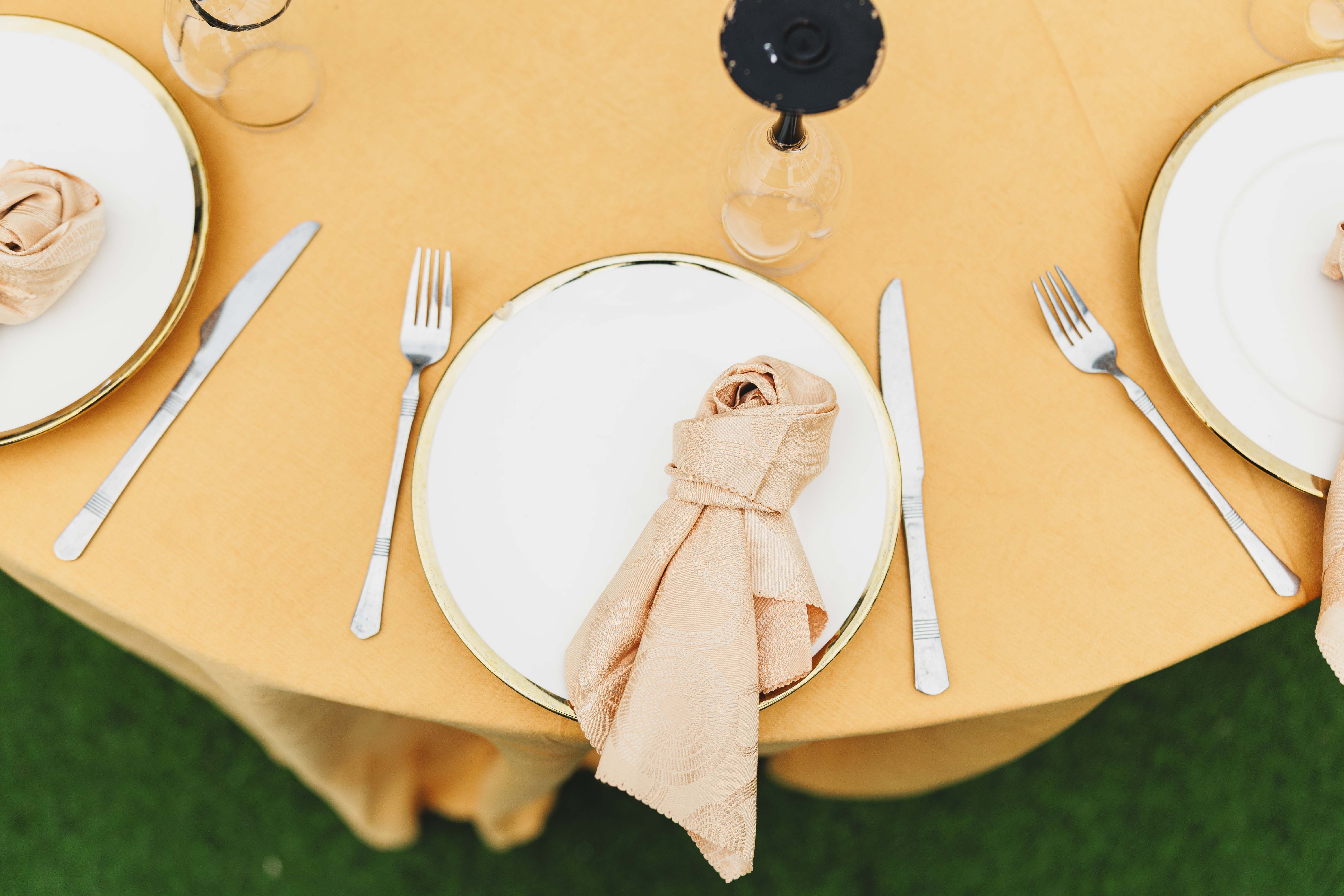 Overhead view of a table setting with a yellow tablecloth, white plates, and neatly folded napkins.