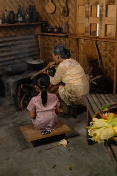 Elderly woman and child cooking in rustic kitchen with traditional methods.