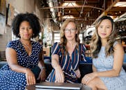 三位职业女性自信地坐在现代化的办公空间里，拥抱多元化和协作