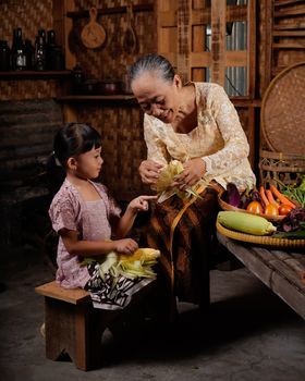 Elderly woman showing young girl how to prepare corn in a traditional kitchen setting.