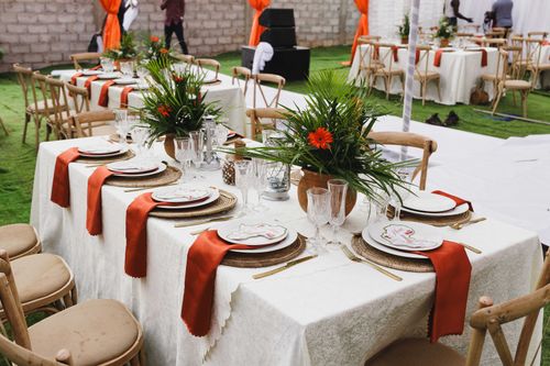Free Elegant outdoor table setup with floral centerpiece, orange accents, and wooden chairs, perfect for weddings or events. Stock Photo
