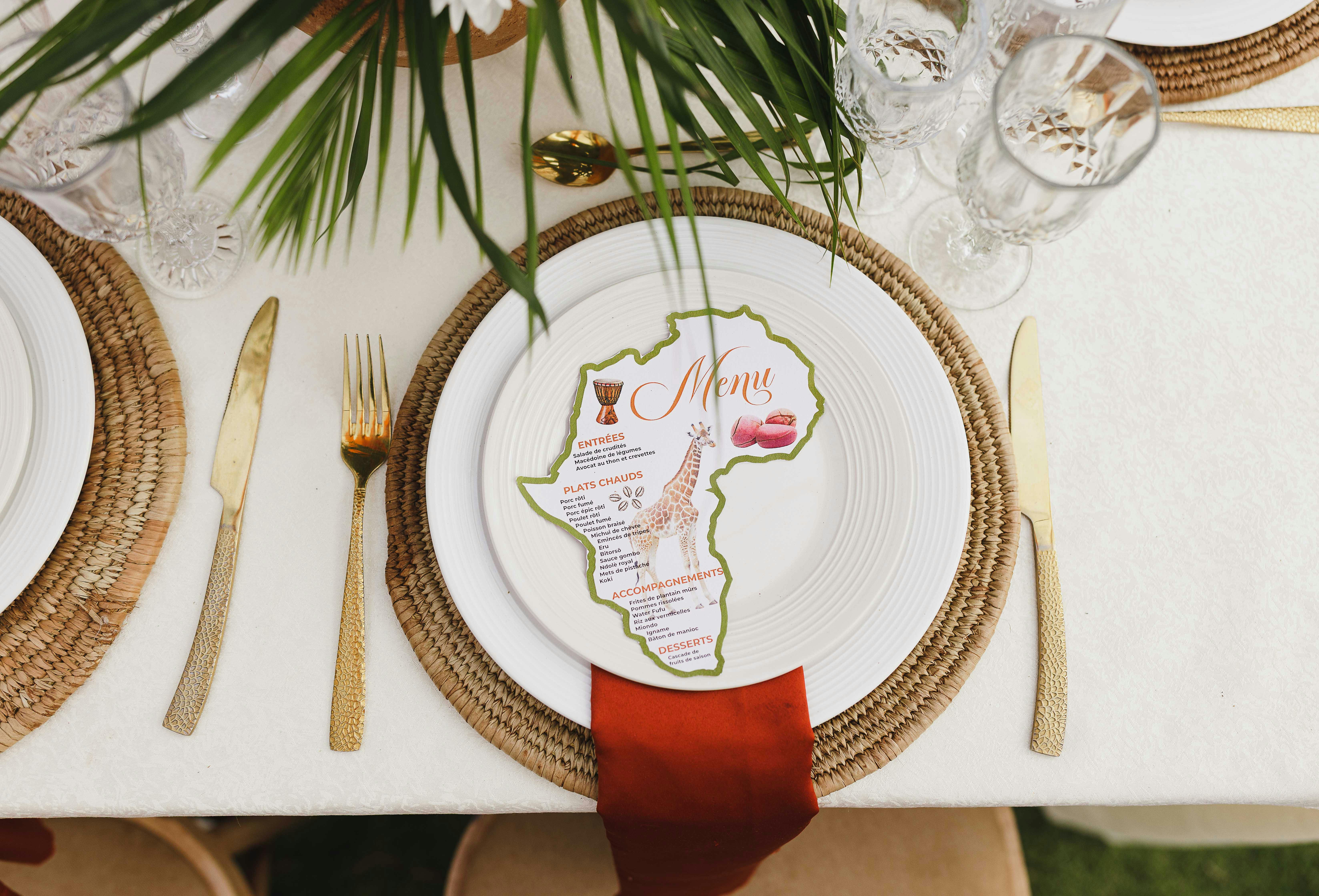 Sophisticated wedding table setting with Africa-shaped menu, gold cutlery, and crystal glassware.