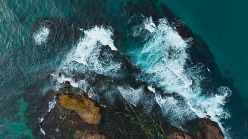 Free Stunning aerial view of waves crashing on a rugged rocky shoreline, showcasing dramatic oceanic scenery. Stock Photo