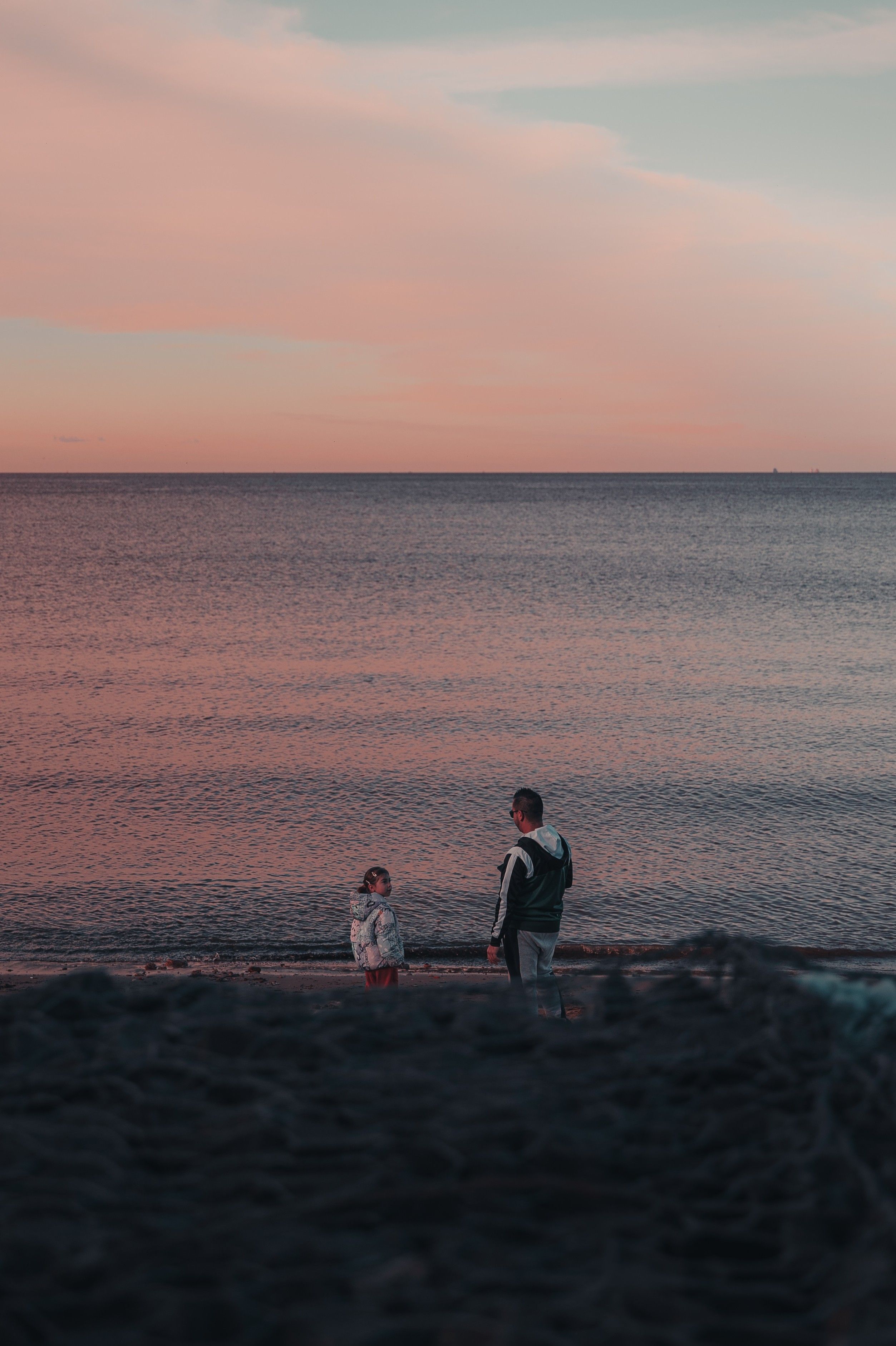 A serene moment of a father and child at the beach during a peaceful sunset.