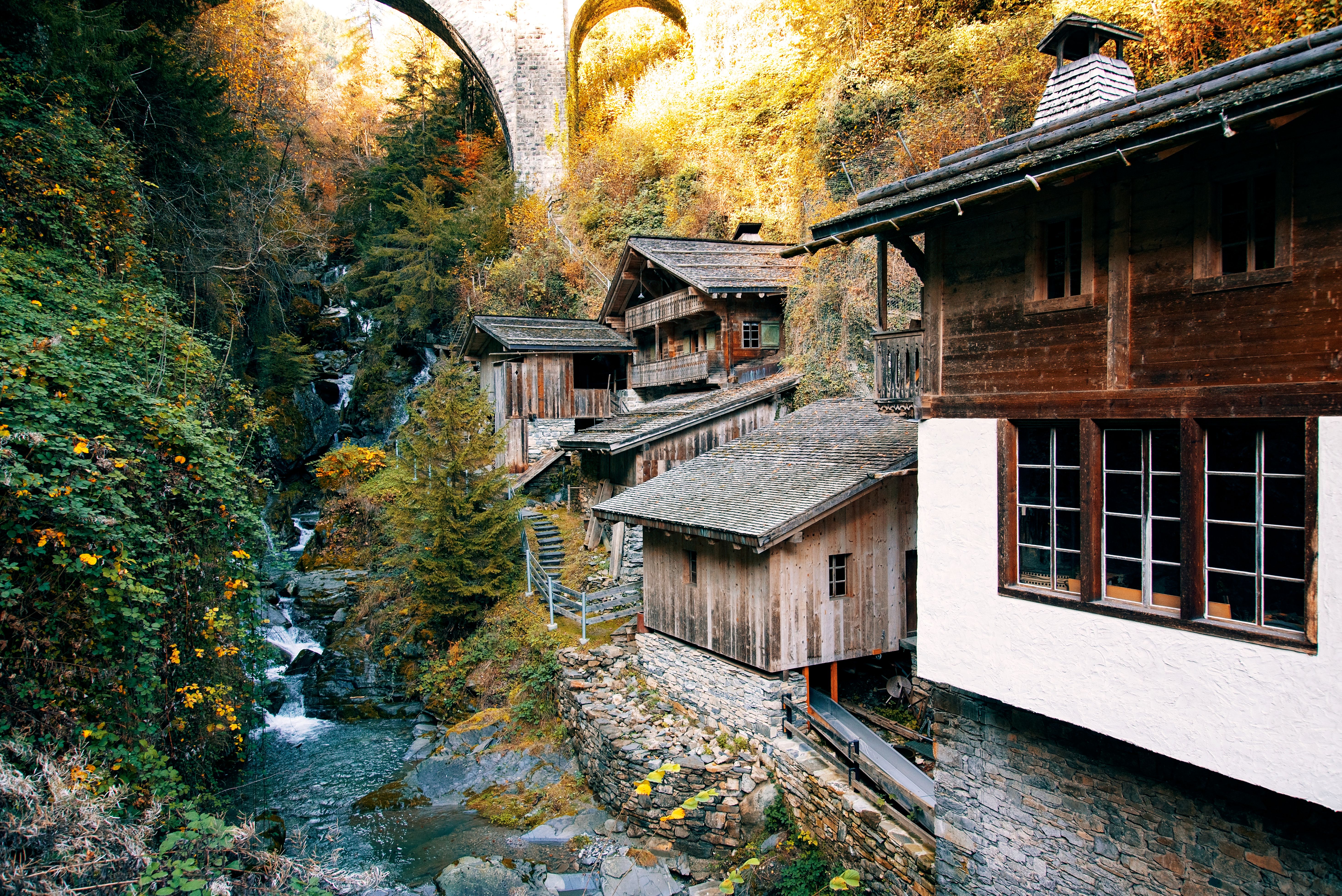 Charming wooden houses in a picturesque mountain village with autumn foliage and a stone bridge.