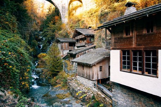 Charming wooden houses in a picturesque mountain village with autumn foliage and a stone bridge.