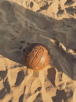 A vintage leather soccer ball resting on a sunny sandy beach, evoking nostalgia and outdoor fun.