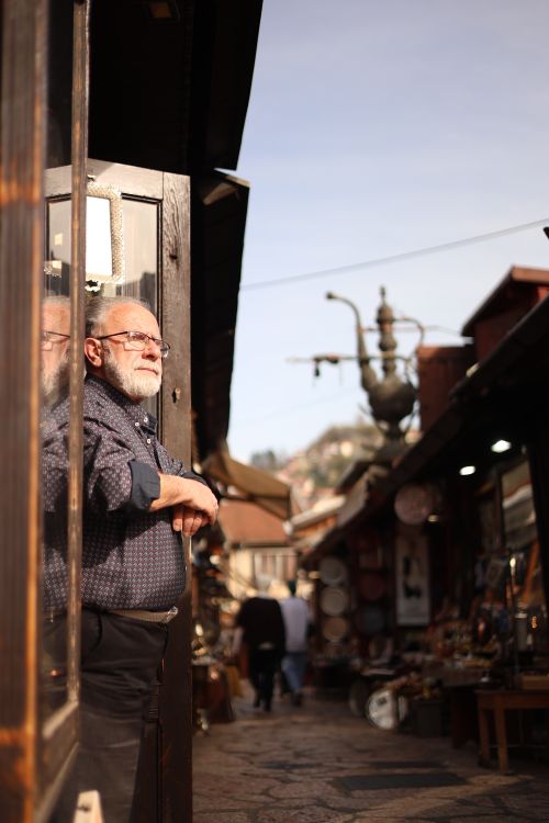 Free Elderly man watches from doorway in vibrant outdoor market, rich cultural atmosphere. Stock Photo