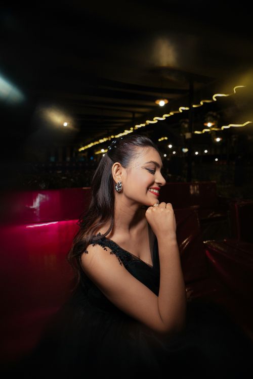 Free A woman in a black dress elegantly poses against a dark, ambient backdrop with soft lighting. Stock Photo